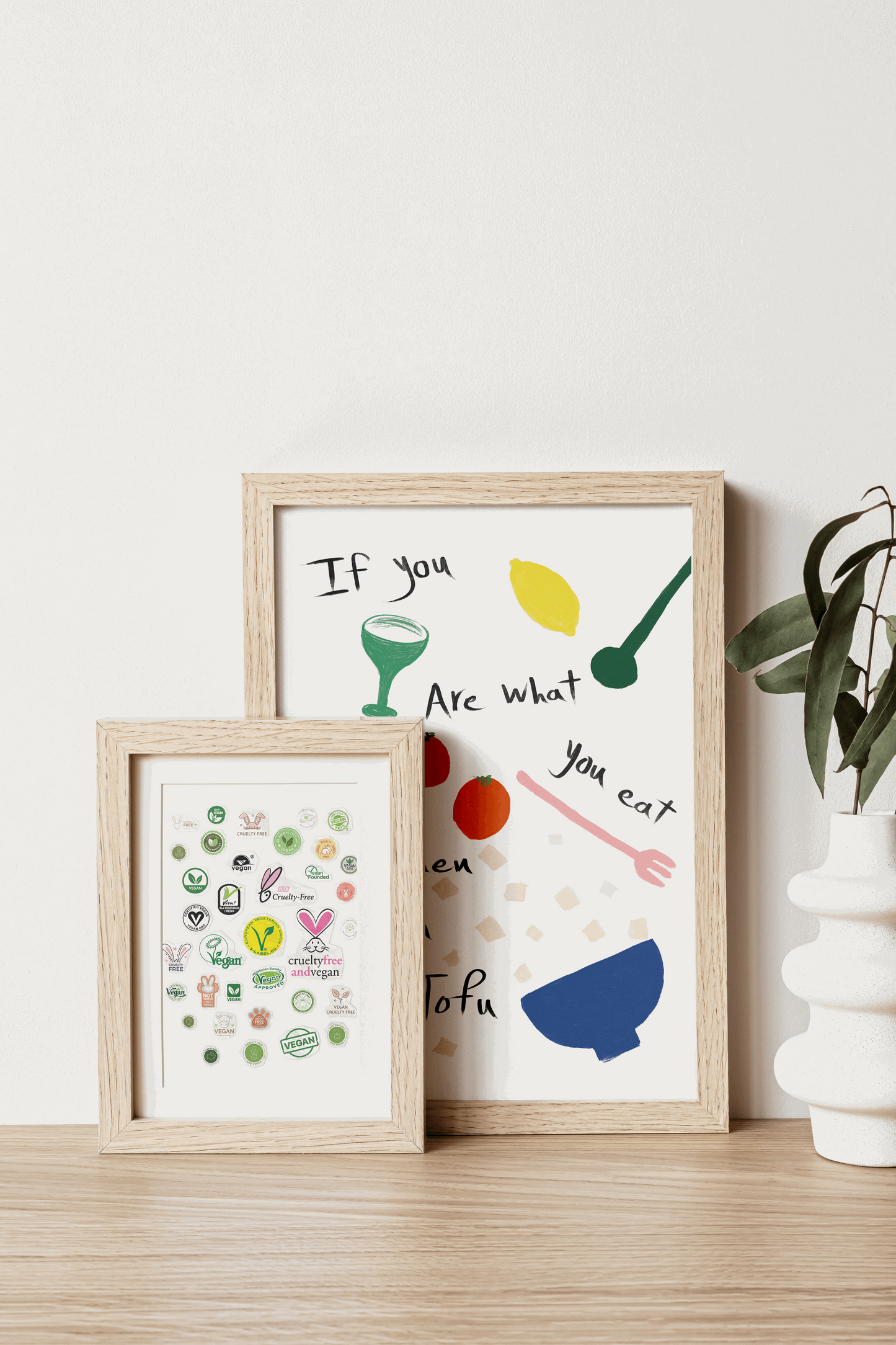 Charming home decor scene with two frames: a larger one with a food and tofu quote, and a smaller one featuring vegan badges, on a wooden table.